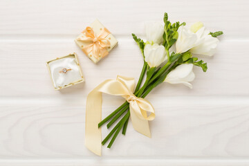 White fresia flower and gift box with diamond ring on wooden background, top view