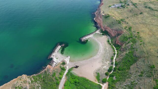 Bolata Beach, Cape Kaliakra, on the northern coast of Bulgaria. The high steep banks of a reddish hue are in harmony with the greenery of grass and the endless blue sea. View from drone.
