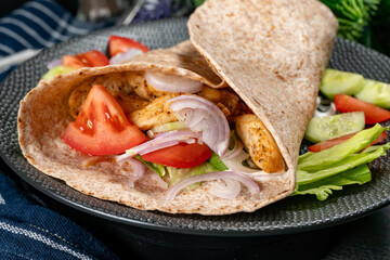 Wholegrain tortilla wraps with vegetables and chicken on a plate.