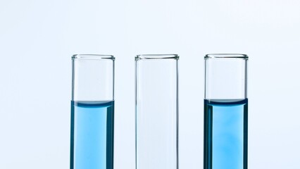 Three glass test tubes on a white background. Two test tubes are filled with blue liquid and one is empty. Concept of medicine, biochemical research. Close-up.