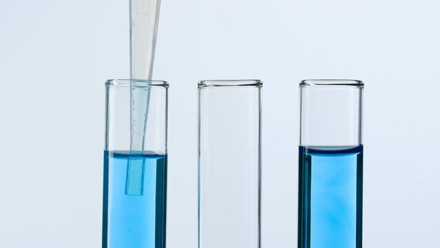 Three glass test tubes on a white background. Two test tubes are filled with blue liquid and a pipette is lowered into one of them. Concept of medicine, biochemical research. Close-up.