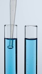 Two glass tubes on a white background. The test tubes are filled with blue liquid, a pipette is lowered into one of them. Concept of medicine, biochemical research. Close-up