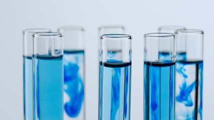 Science and biotechnology creative concept. Close up of laboratory glassware on white background. Test tubes with transparent and blue liquid and dissolving cloud of blue substance. - Powered by Adobe