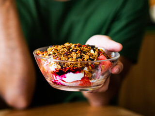A man hand holding granola bowl with dried oats, nuts seeds muesli, cubes watermelon tropical fruit...