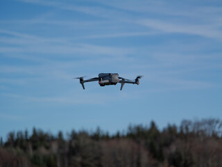 Drohne im Flug vor blauem Himmel und WaldgebietDrohne im Flug vor blauem Himmel und Waldgebiet