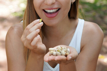 Fitness healthy girl outdoors. Close up of young woman eating pistachios in the park. Selective focus on her mouth.