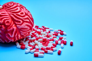 Red brain with a pile of red and white pills, on a blue surface. Concept of addictions.