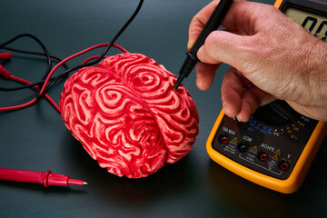 Man's hand attaching electrodes to a red fake human brain on a dark green background.
