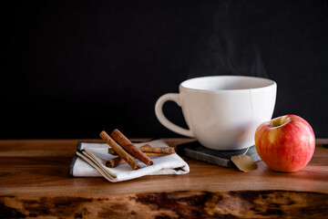 White tea mug with warm tea with apple slice and cinnamon sticks on wooden table with mulling spices