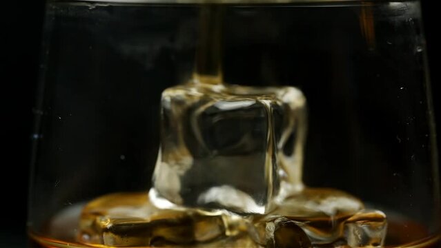 Whiskey is poured into a glass with ice on a black background close