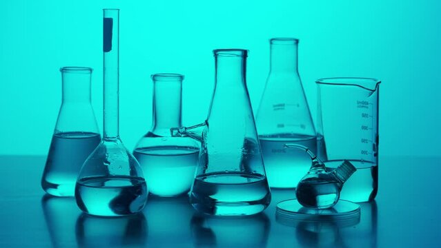 Close up medical glassware on neon background. Laboratory table with many different beakers and test tubes with liquid for experiments in blue neon light.