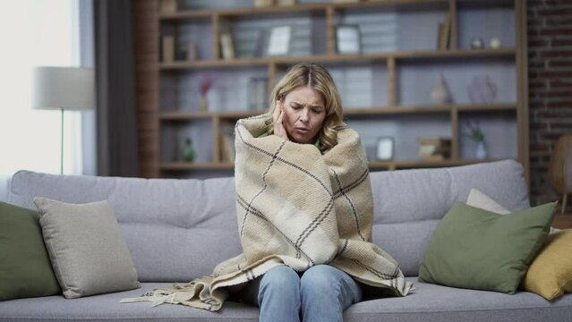 Mature woman is frozen at home and covers a blanket. It is cold in apartment flat or house. Heating does not work Covered female with plaid freezing feeling cold low temperature at home indoor