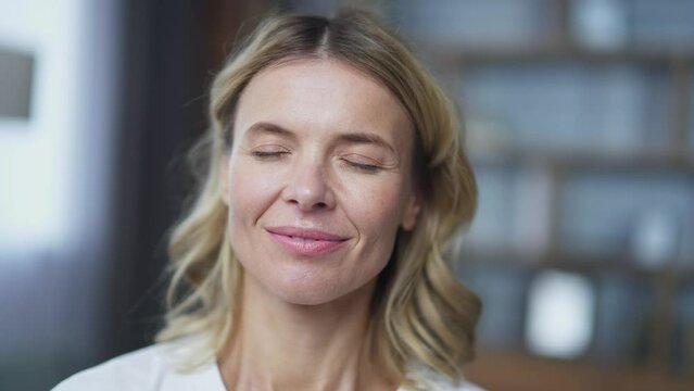 Close up face mature woman meditating with eyes closed sitting in lotus position on sofa in living room at home. Calm female in rest relaxes doing yoga breathing exercises after working day
