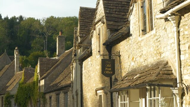 CLOSE UP: Beautiful facades and roofs of old houses made from honey coloured stone. Picturesque countryside village of Castle Combe with charming terraced cottages under green hill on a sunny day.