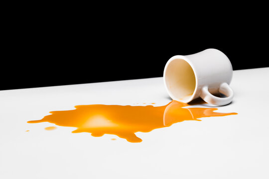 A large amount of creamed coffee spilling from a white restauraunt-style mug on a white table against a black background