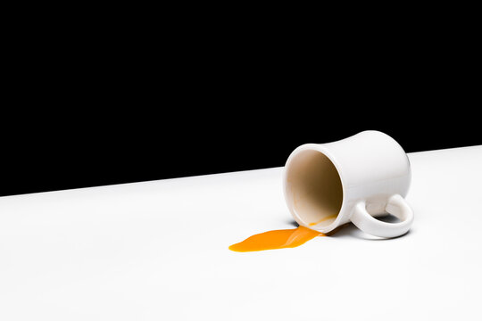 Creamed coffee spilling from a white restauraunt-style mug on a white table against a black background