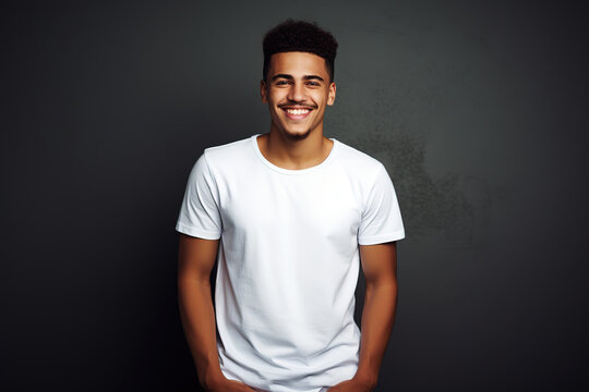 Happy Hispanic young man in blank white t-shirt on black background. Smiling Latin American man t-shirt mock up template for design print
