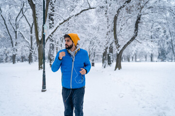 Young determined handsome man running in city park at cold winter day and listening to music on his...