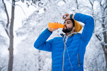 Tired man athlete taking a break drinking water while exercising in winter.