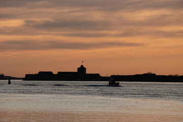 Obraz premium Silhouettes of an old coastal fort and a small boat at sunset.