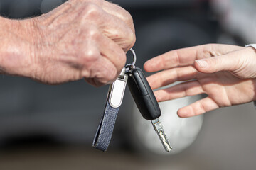 A businessman hands over a car key to a woman in front of a blurred car