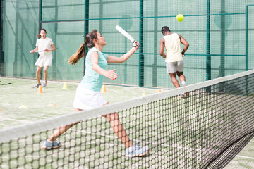 Happy woman learning to play padel game on tennis court outdoor. Other athletes are training in the...