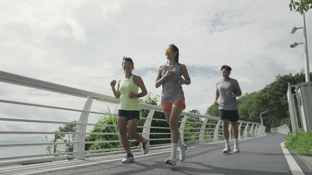 three happy young asian people jogging running exercising outdoors in park by the sea