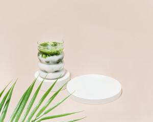 Iced matcha latte on pedestal next to empty pedestal with palm leaf