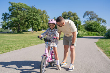 Father teaching daughter to ride bike in park