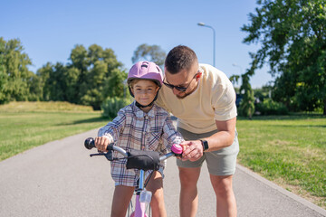 Father teaching daughter to ride bike in park