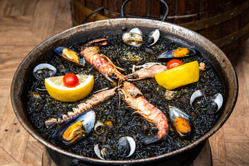 Traditional black paella with seafood and lemon in a large pan