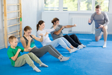 Mom, dad and children athletes of martial arts section in sitting position perform exercises that...