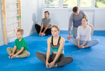 Obraz premium Cheerful family, parents with children athletes before training martial arts performs stretching butterfly exercise. Modern positive family chooses active hobby and leisure activity.