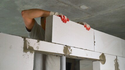 The mortar is applied to the wall masonry block. Construction worker laying blocks. Applying an...