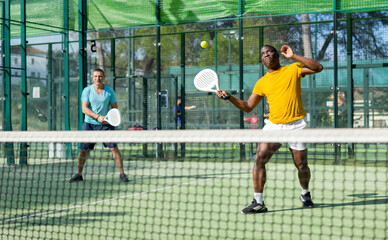 Sporty african american man padel tennis player trains on the court with a partner using a racket...