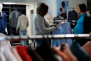 Clothing store employee and pregnant woman customer checking shirt, examining size and style....