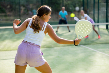 Sporty European woman playing padel tennis during a friendly doubles match on an outdoor court