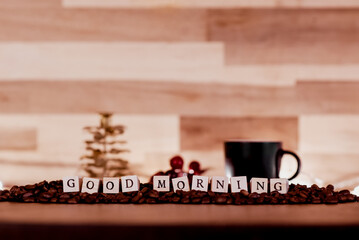 Letter cubes forming ‘Good morning’, surrounded by coffee beans and some accessories on a wooden backdrop