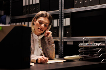 Woman investigator having remote discussion with inspector using landline phone, trying to solve...