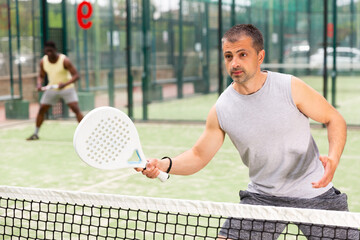 Male players playing padel in a padel court outdoor behind the net