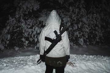 A girl soldier in winter camouflage with an AK 12 assault rifle behind her back in snowy forest ,...