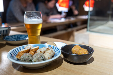 Japanese dumplings and fish ball on a plate with a glass of beer.

