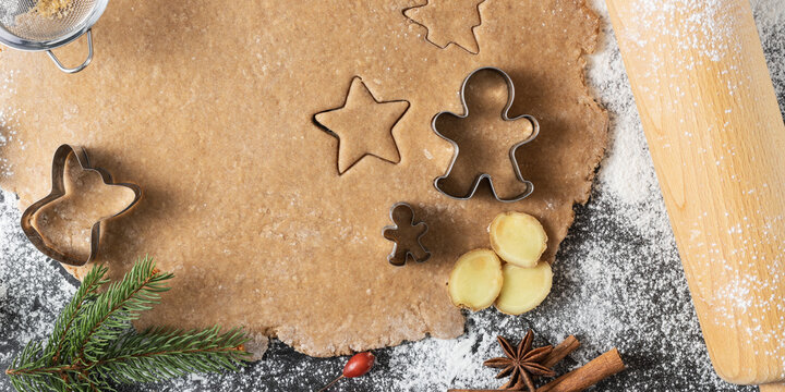 Fresh homemade dough for preparation christmas gingerbread cookies and baking cutters on scattered flour with decor.