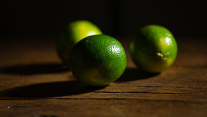 Lime arranged on a wooden board, set against a dark and dramatic background, illuminated by hard light, casting distinct shadows.