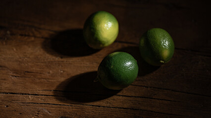 Lime arranged on a wooden board, set against a dark and dramatic background, illuminated by hard light, casting distinct shadows.