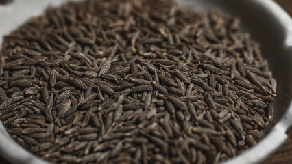 Cumin seeds in a bowl on wooden background. Close up.
