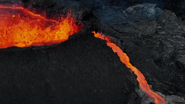 Erupting volcano, red hot magma boiling and splashing out a crater, making lava flows, drone close up shot. Concepts of volcanic activity, climate change, and nature.