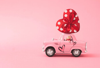 Love composition made of Pink toy car delivering gift box in the shape of a heart with ribbon and...