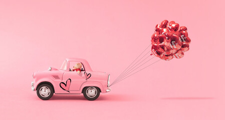 Love composition made of Teddy bear and Pink toy car delivering a bouquet of balloons on pink background. Minimal concept of Valentine's Day or love. Creative art, minimal aesthetics.