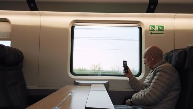 Adult pensioner traveling by train alone and taking photos of the landscape 